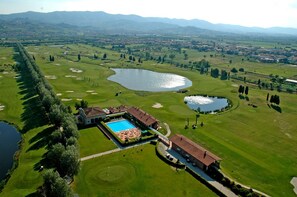 An aerial view of a golf course with a swimming pool, a clubhouse, and a lake. - Hotel Giardino (Prato)