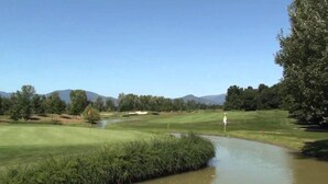 A golf course with a water body, trees, and distant mountains. - Hotel Giardino (Prato)