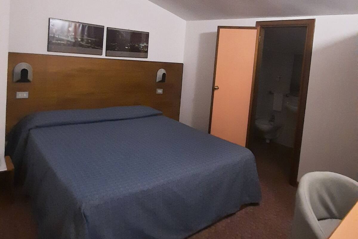 A small, simple room with a single bed, a desk, and a door leading to a bathroom.
