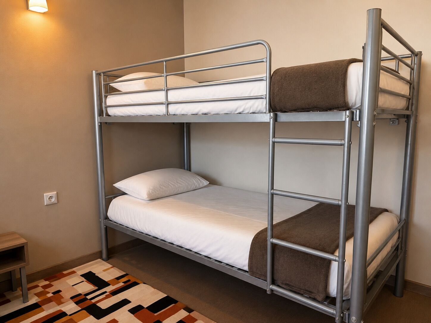Una cama individual con estructura metálica, ropa de cama blanca y una manta marrón.