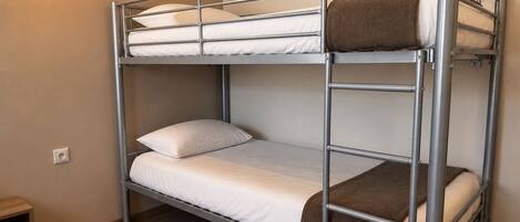 Una cama individual con estructura metálica, ropa de cama blanca y una manta marrón.