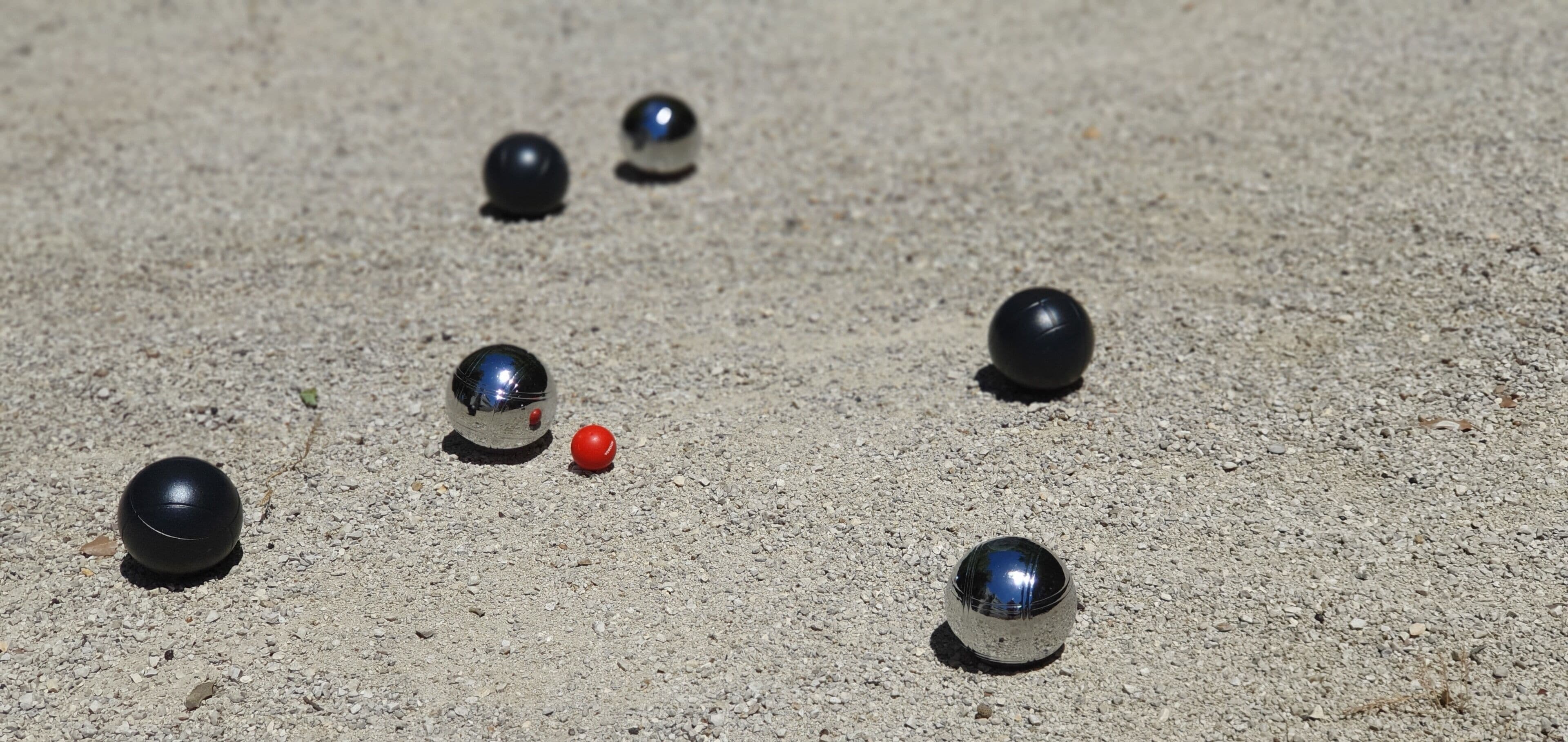 Une série d’objets sphériques noirs et rouges posés sur une surface de gravier.