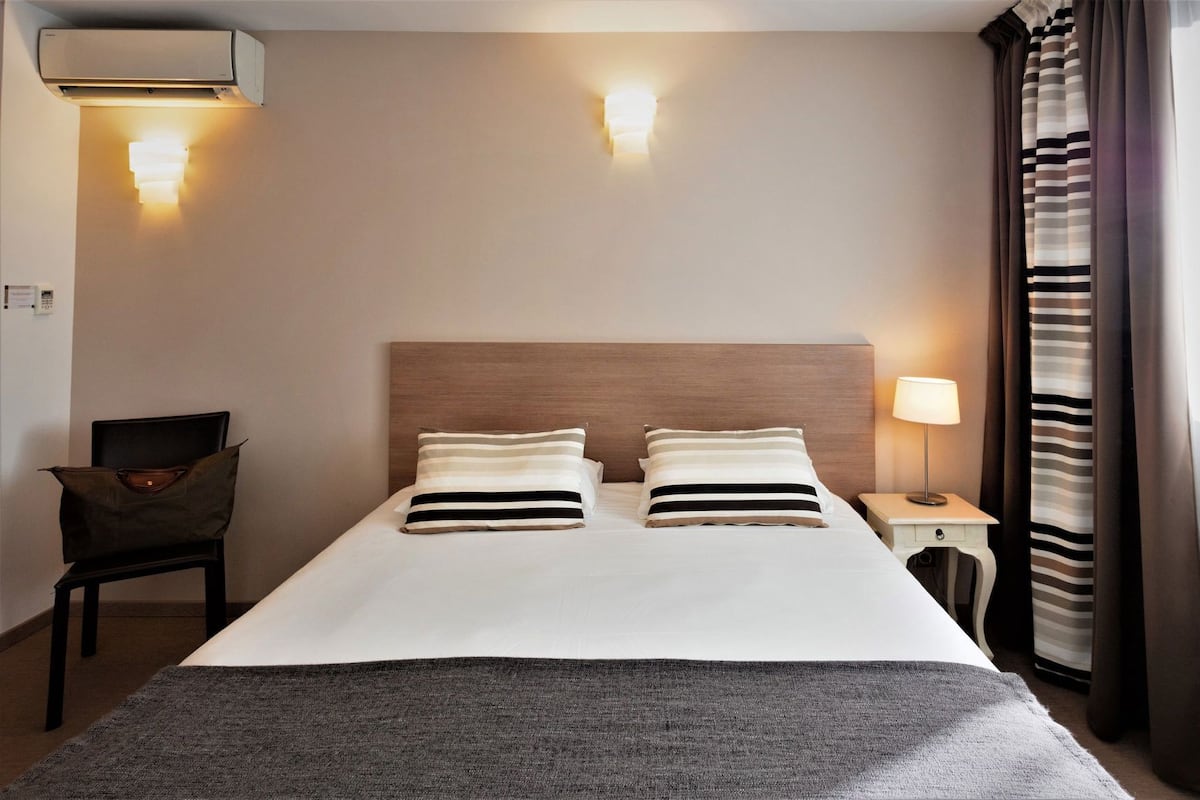 Ein Hotelzimmer mit einem Bett, einem Nachttisch mit Lampe, einem Sessel und einer Wand-Klimaanlage.