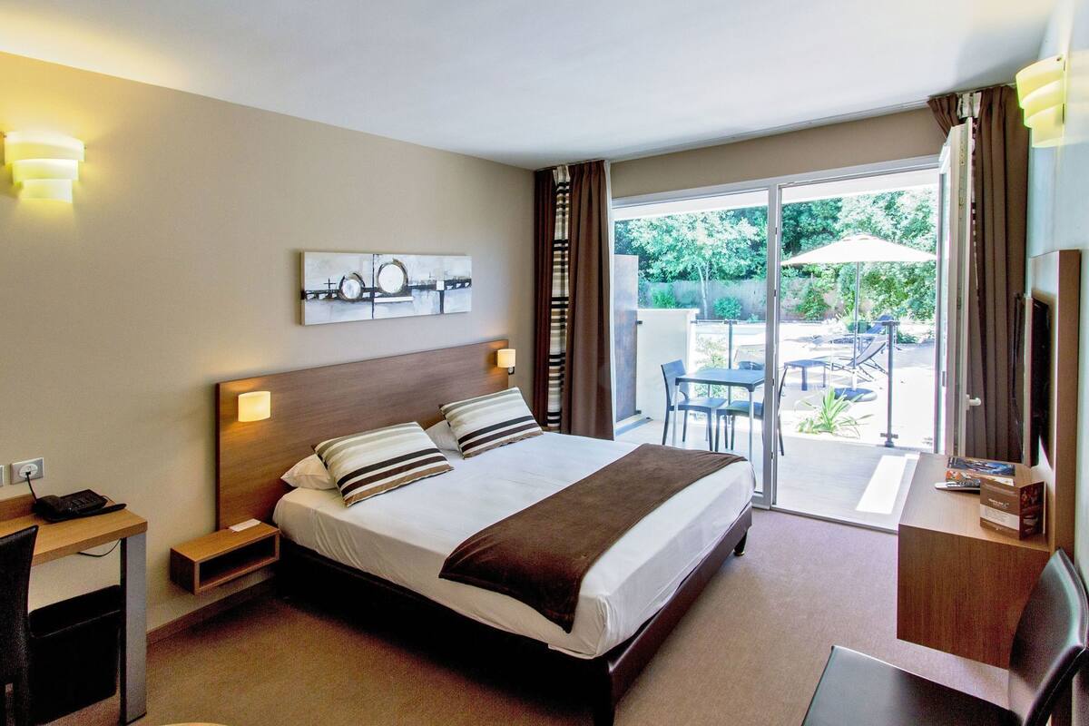 Ein Hotelzimmer mit Bett, Nachttischen, Schreibtisch, Fernseher und Blick auf die Terrasse.