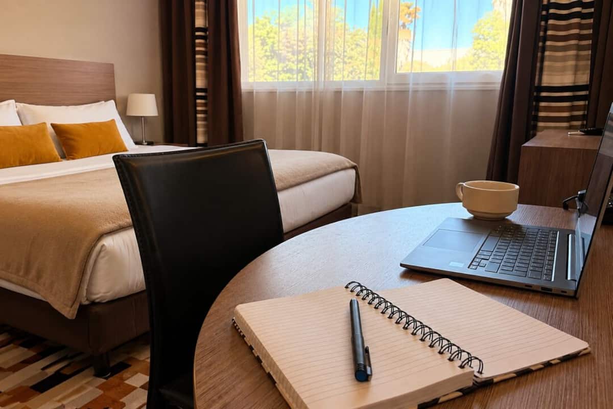 Ein Hotelzimmer mit einem Bett, einem Schreibtisch, einem Laptop, einem Notizbuch und einem Stift.