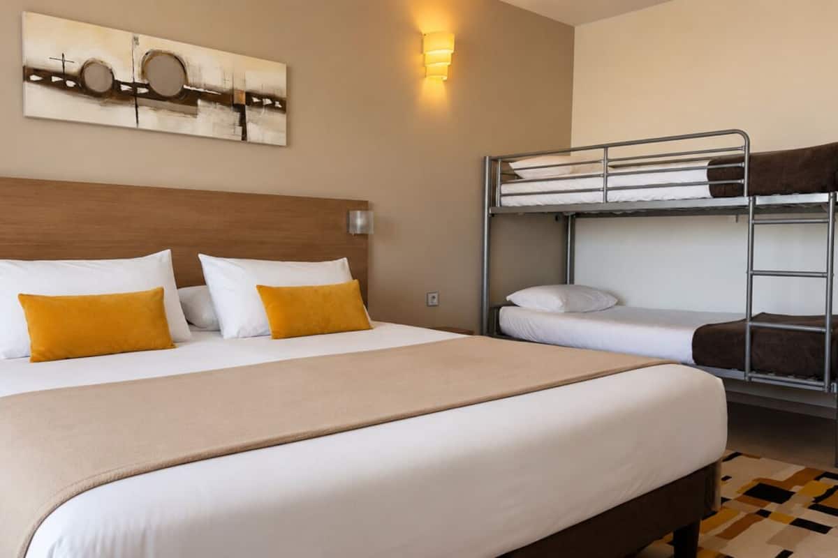 Ein Hotelzimmer mit einem großen Bett, einem Stockbett, einem Holzkopfteil, einem Wandbild und einem gemusterten Teppich.