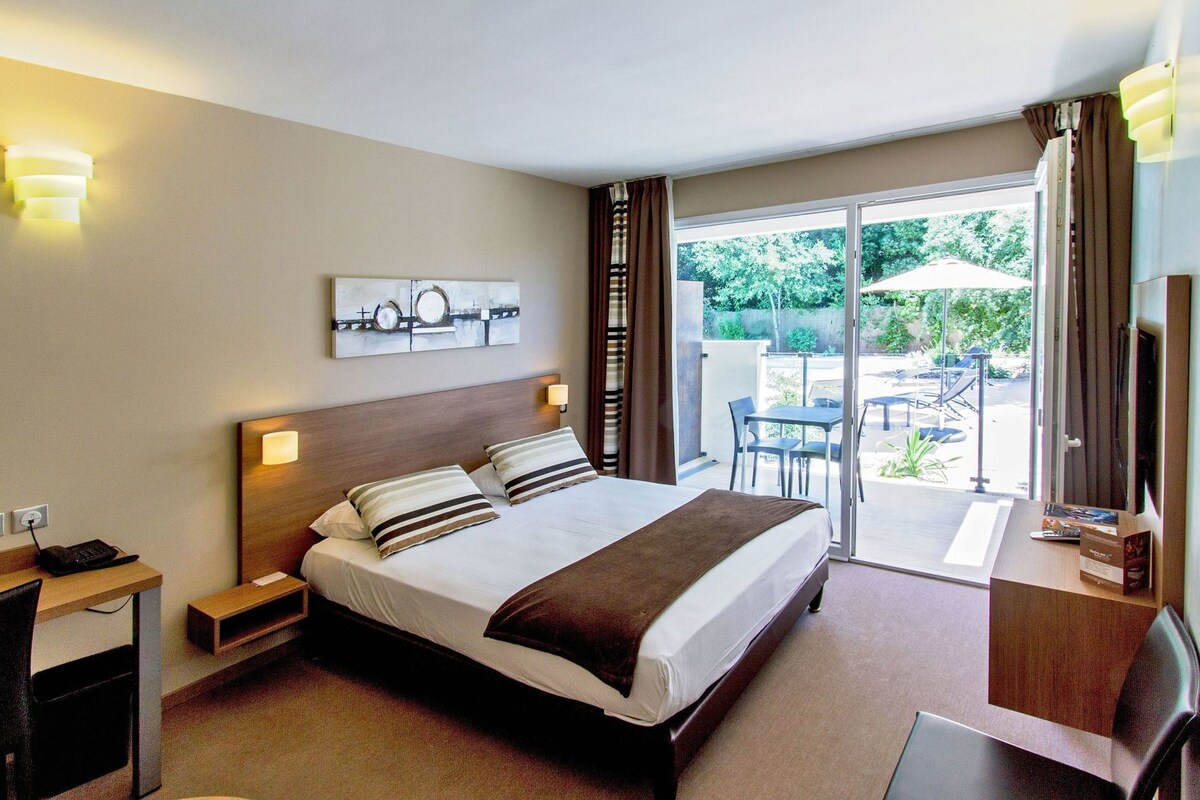 A hotel room with a bed, bedside tables, a desk, a TV, and a view of the outdoor patio.