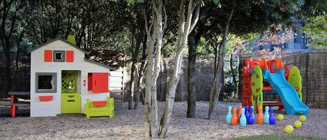 Zona infantil con una casita, un tobogán y una estructura para escalar.