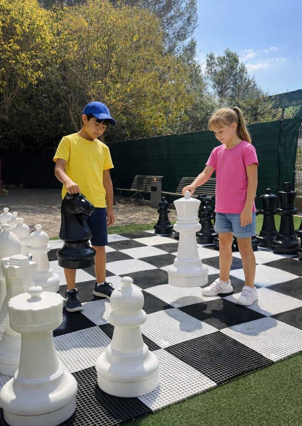 Dos personas jugando un ajedrez gigante sobre un suelo exterior cuadriculado.