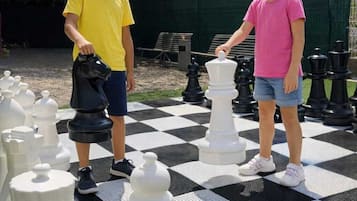 Dos personas jugando un ajedrez gigante sobre un suelo exterior cuadriculado.