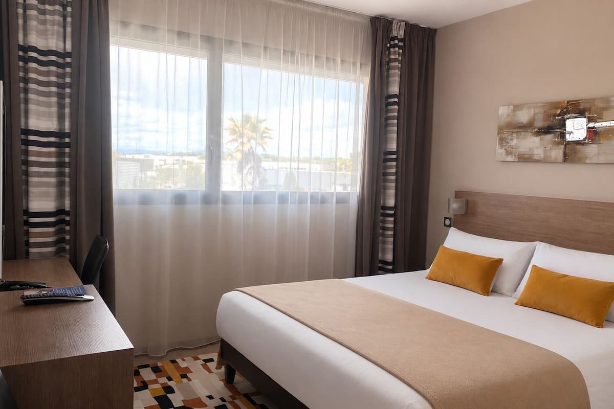 Ein Hotelzimmer mit Bett, Schreibtisch, Stuhl, Fernseher und einem fenster mit Vorhängen.