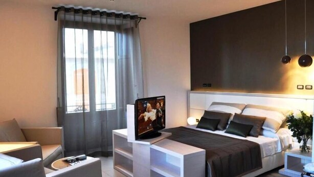 Een moderne hotelkamer met een bed, nachtkastje, televisie en een raam met gordijnen.