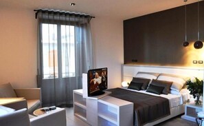 Ein modernes Hotelzimmer mit Bett, Nachttisch, Fernseher und einem Fenster mit Vorhängen.