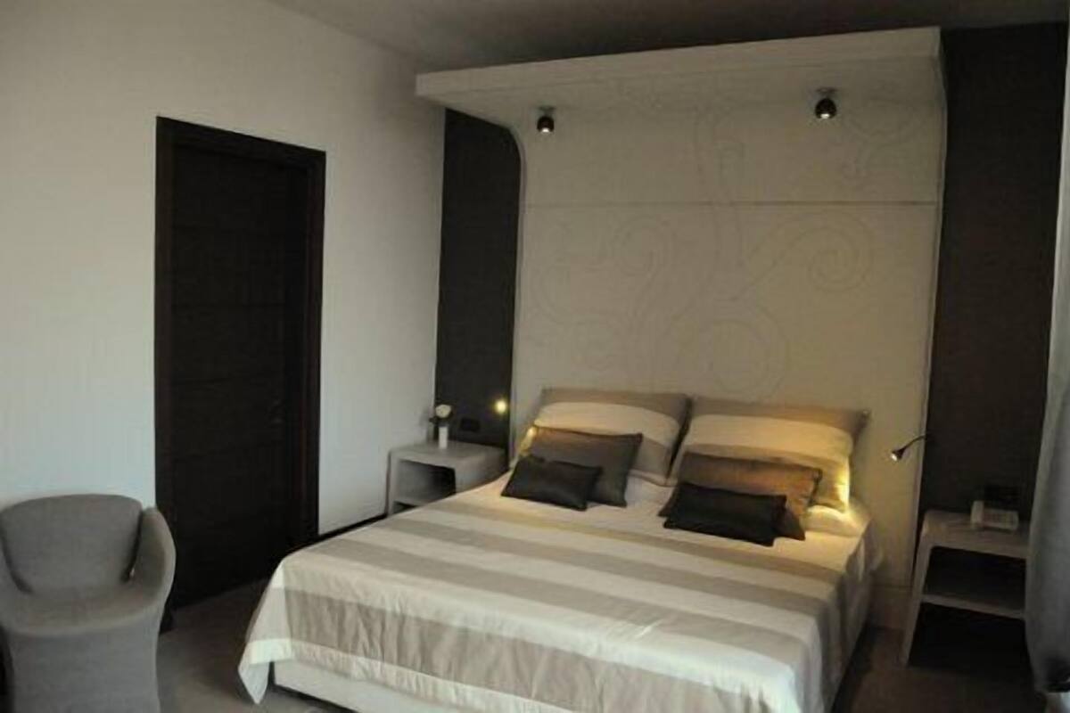 Een slaapkamer met een bed, nachtkastjes, een stoel en een deur.