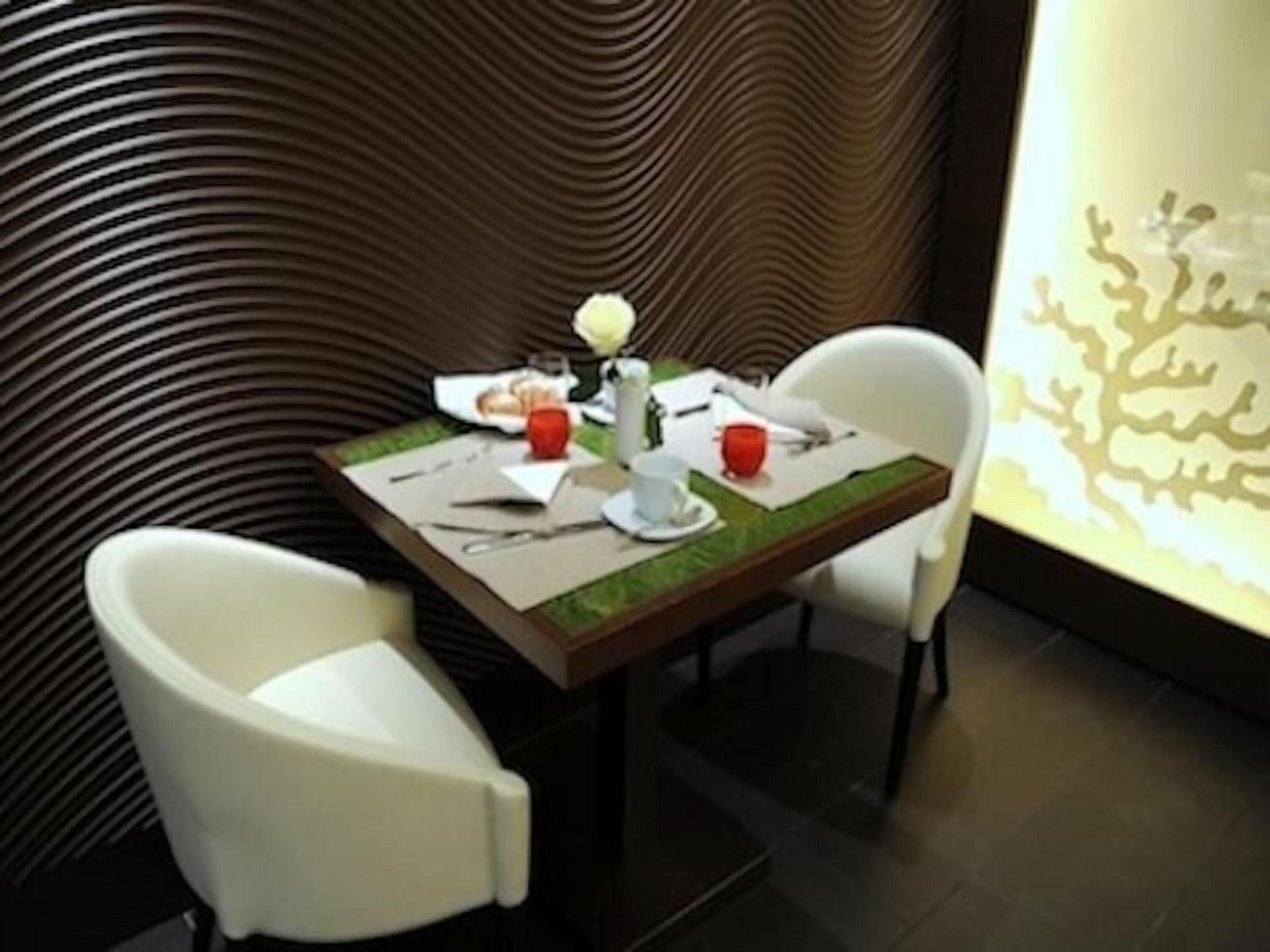 A dining area with a table set for two, featuring a modern design with a patterned wall and a decorative light fixture.