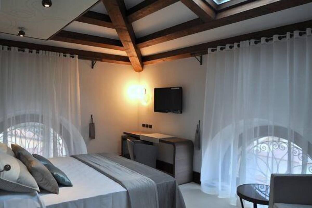 Een slaapkamer met een bed, een bureau en een stoel. Er hangt een televisie aan de muur.