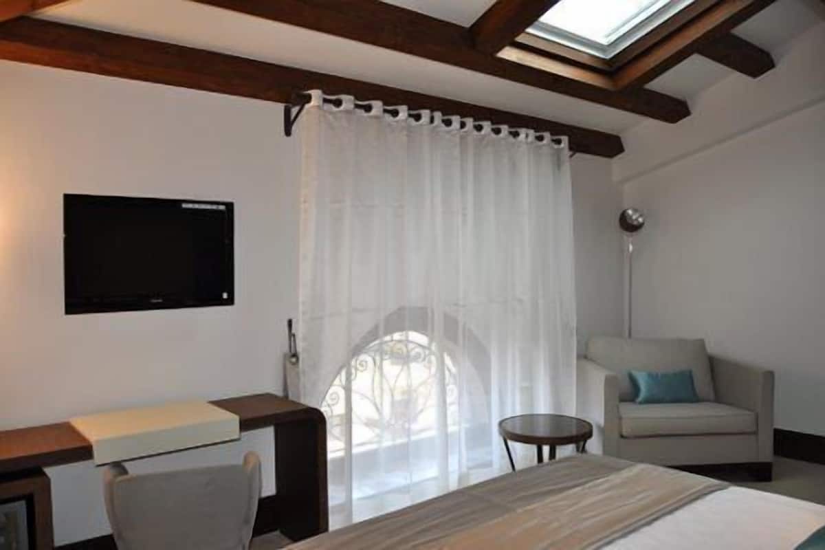 Hotelkamer met een bed, bureau, stoel, bank, televisie aan de muur en raam met gordijn.