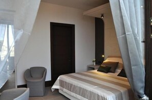 A modern bedroom with a bed, a chair, and a door. - Hotel Palazzo Fortunato (Sant'Agata di Militello)