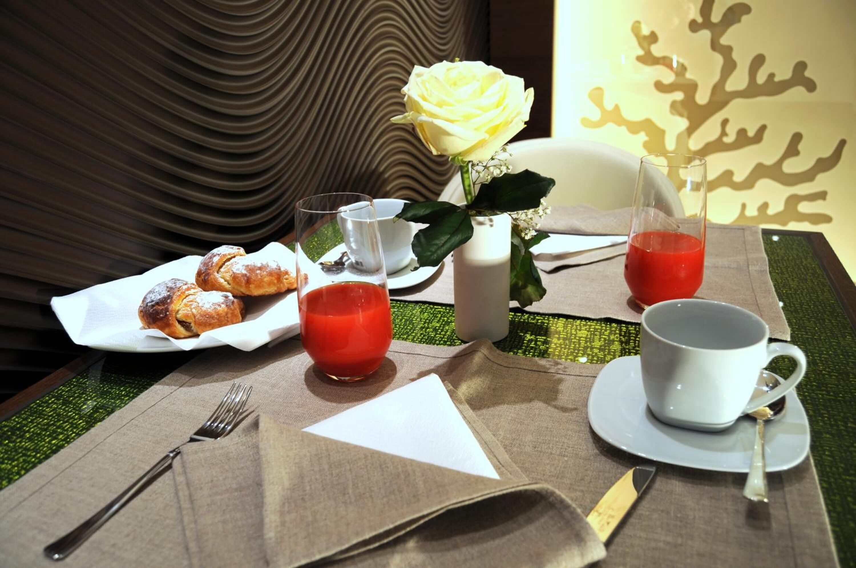 A table set with pastries, a glass of red juice, a white mug, and a vase with a yellow rose.
