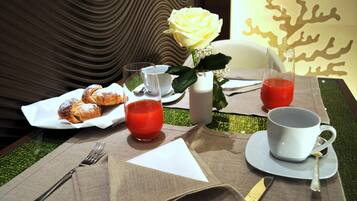 A table set with pastries, a glass of red juice, a white mug, and a vase with a yellow rose.