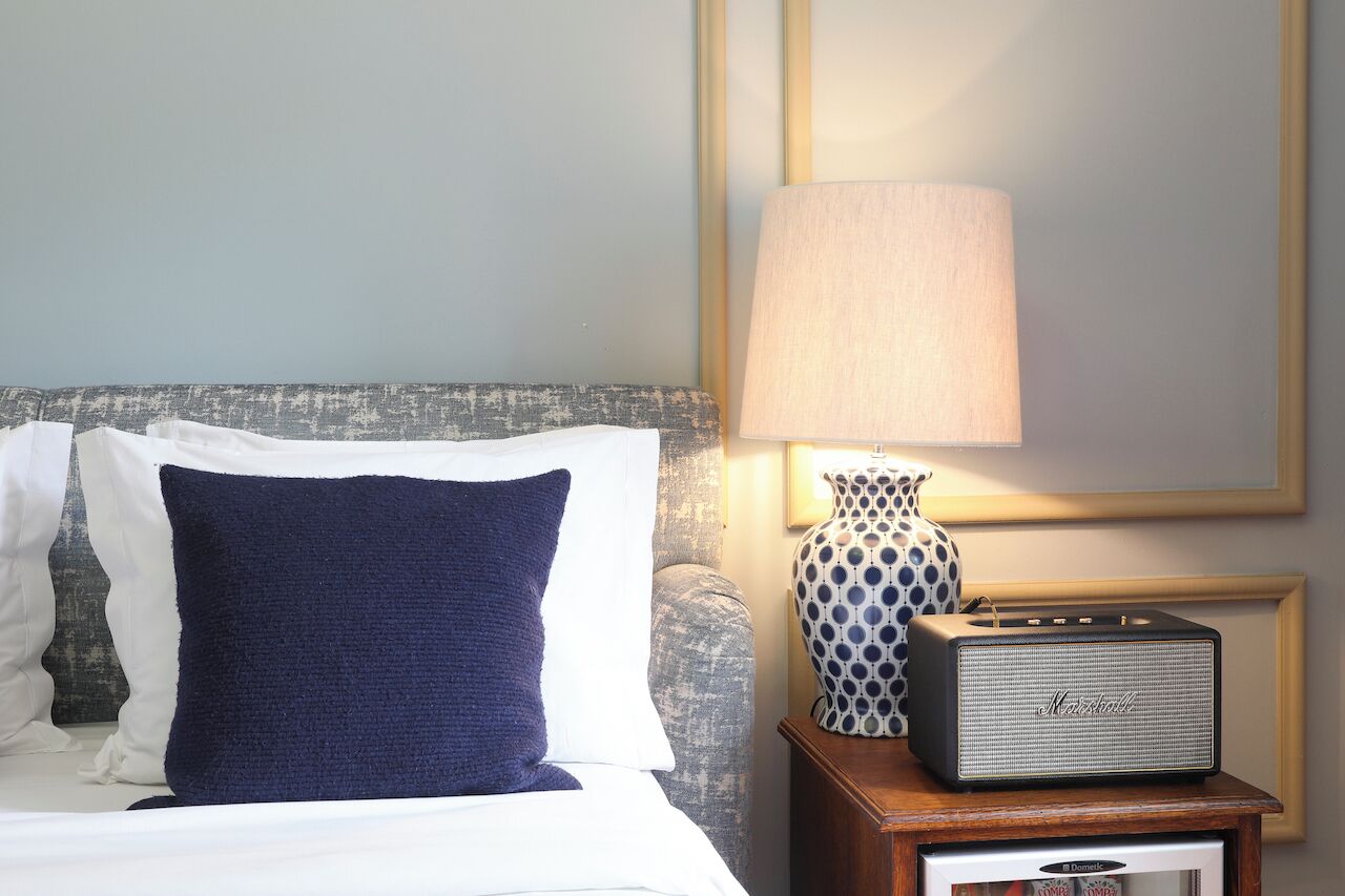 A neatly made bed with a blue pillow, a lamp, and a Marshall radio on a bedside table.