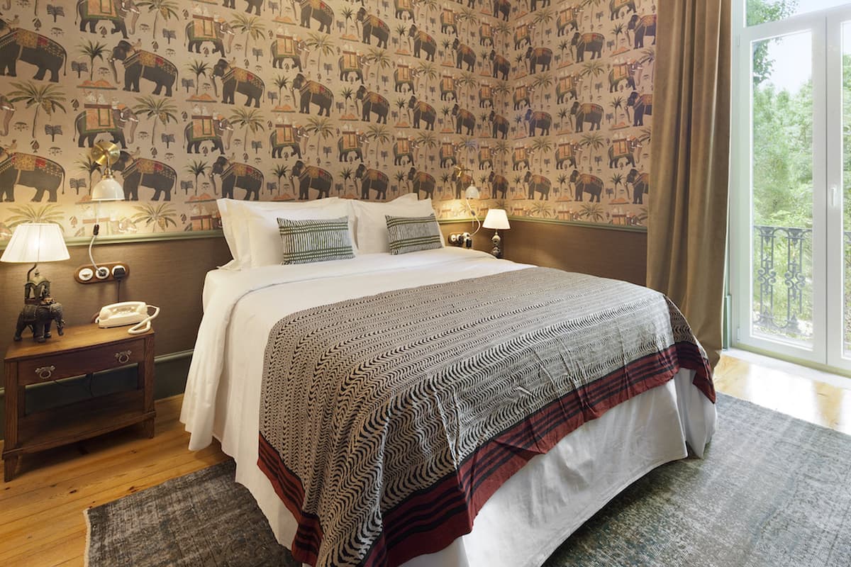 A hotel room with a large bed, two bedside tables, a nightstand, and a view of the outdoors.