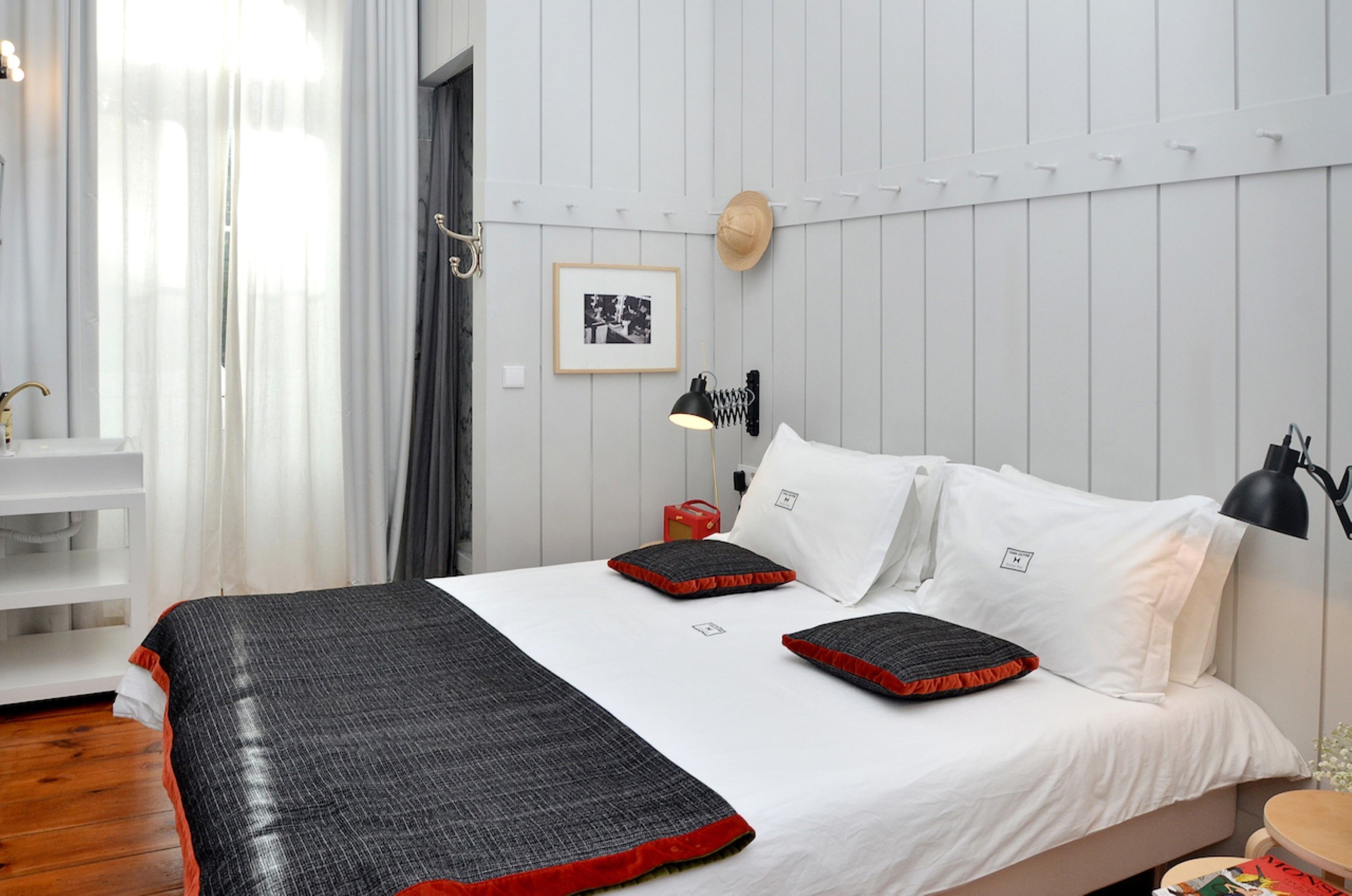 Une chambre à coucher bien rangée, avec un lit, des oreillers, une lampe de chevet, un chapeau accroché au mur et un tableau encadré.