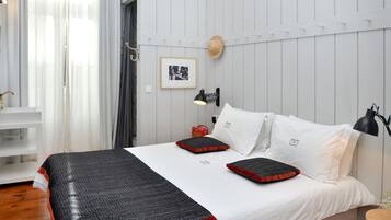 Une chambre à coucher bien rangée, avec un lit, des oreillers, une lampe de chevet, un chapeau accroché au mur et un tableau encadré.