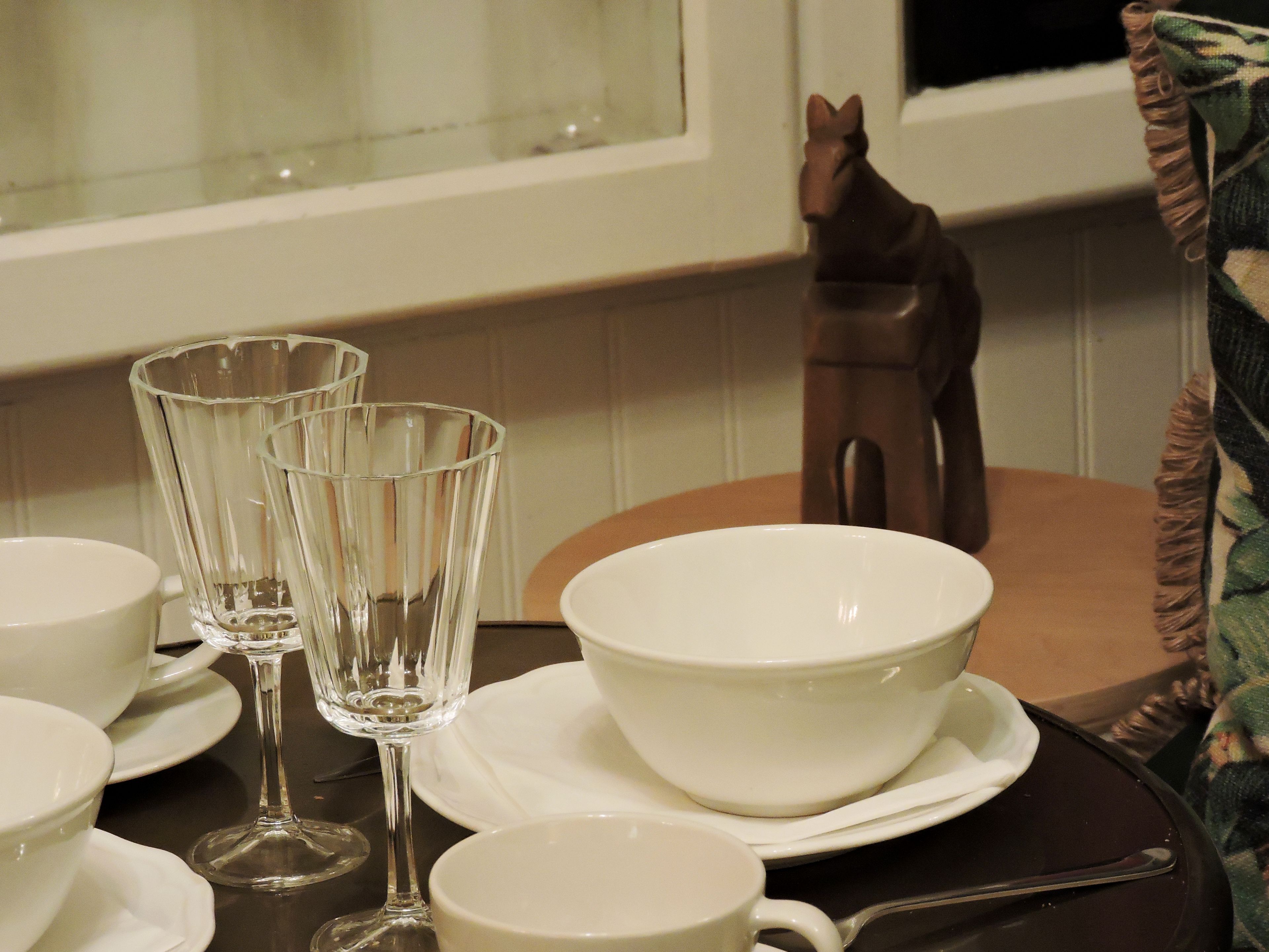 Une table à manger dressée avec des bols, des assiettes et des verres à vin, le tout de couleur blanche.