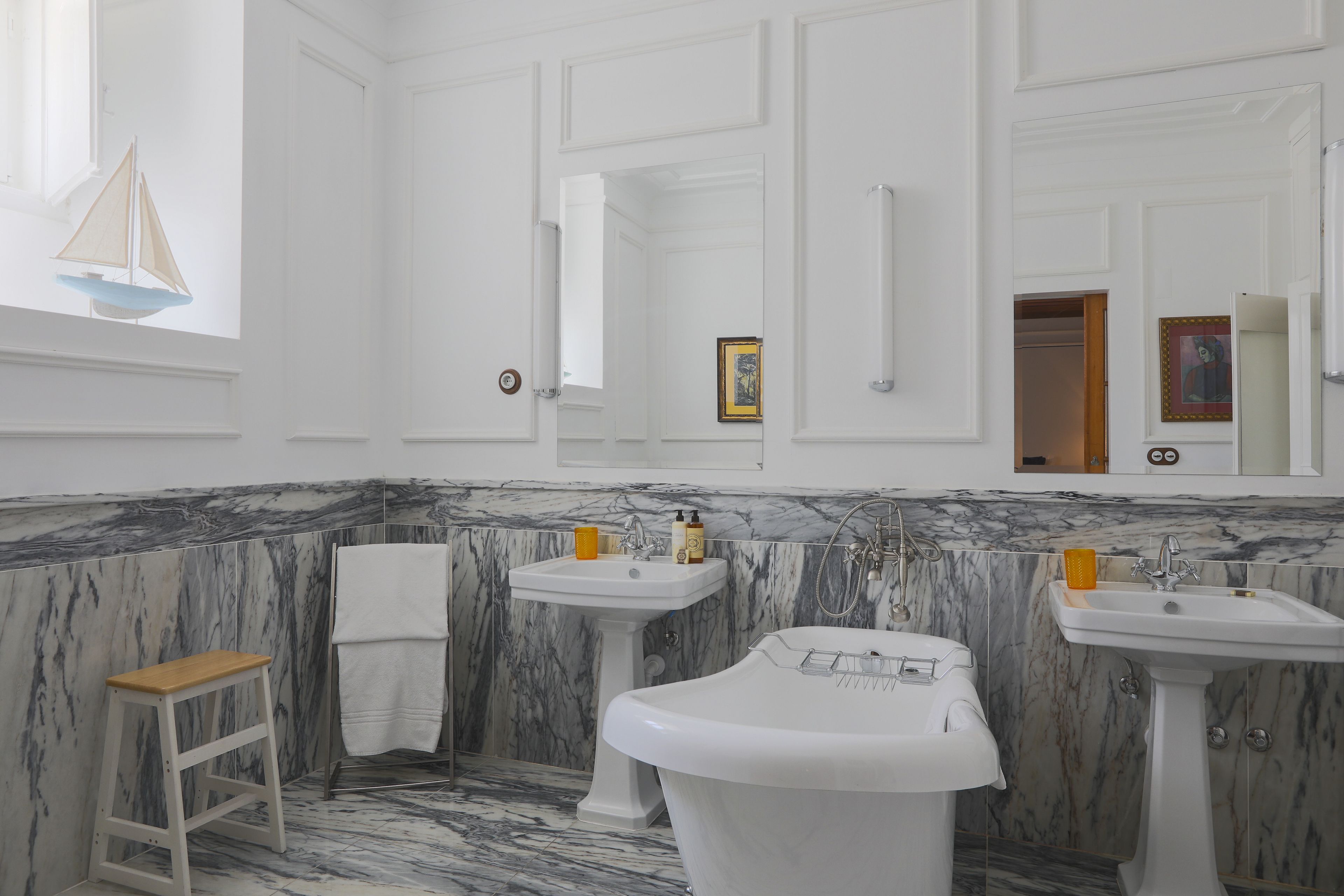 A bathroom with marble walls, two sinks, a bathtub, and a wooden stool.