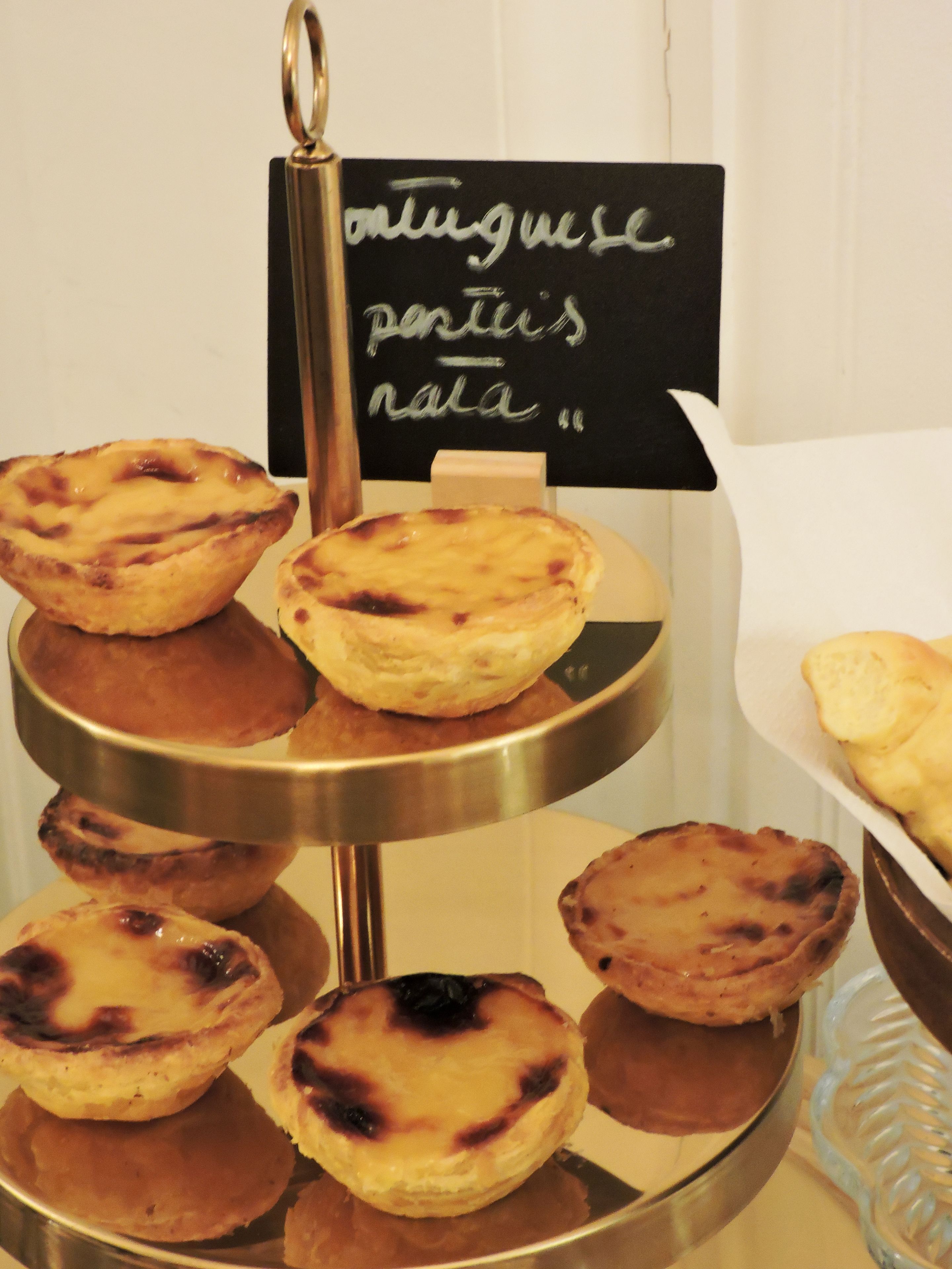 Een drijvlak display van Portugese gebakjes, waaronder vullingstaartjes, op een glanzend metalen standaard.