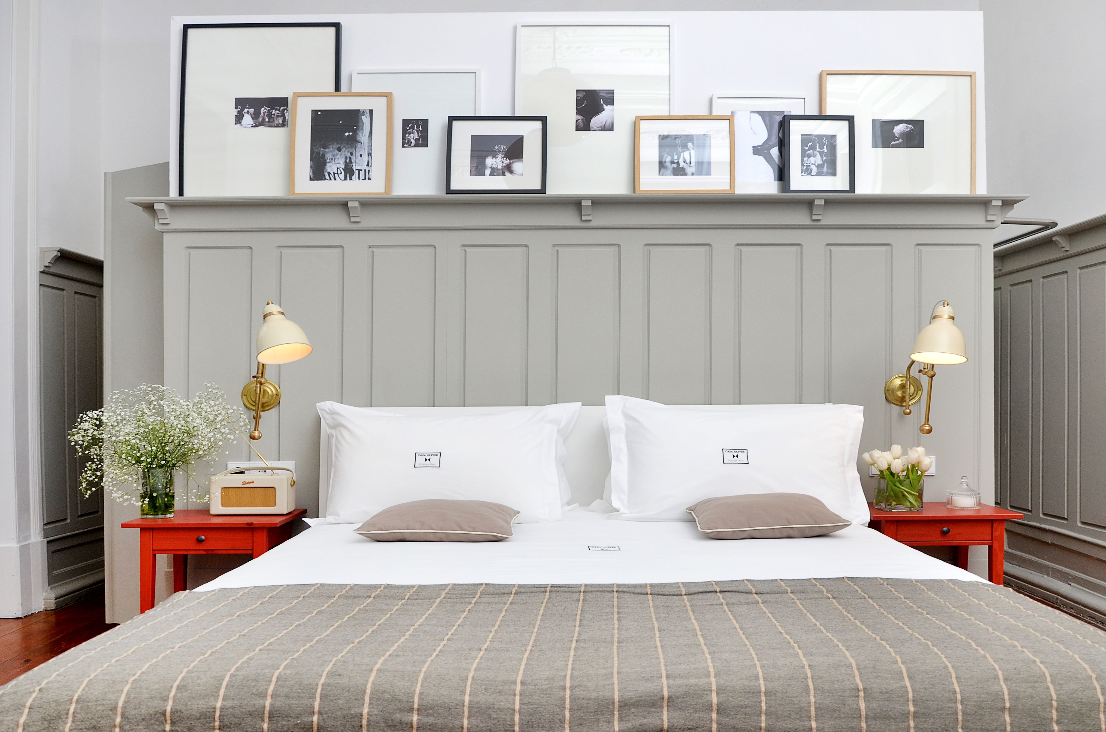 Une chambre à coucher bien rangée, avec un lit, deux tables de chevet, une étagère murale ornée de photos encadrées et une lampe décorative.