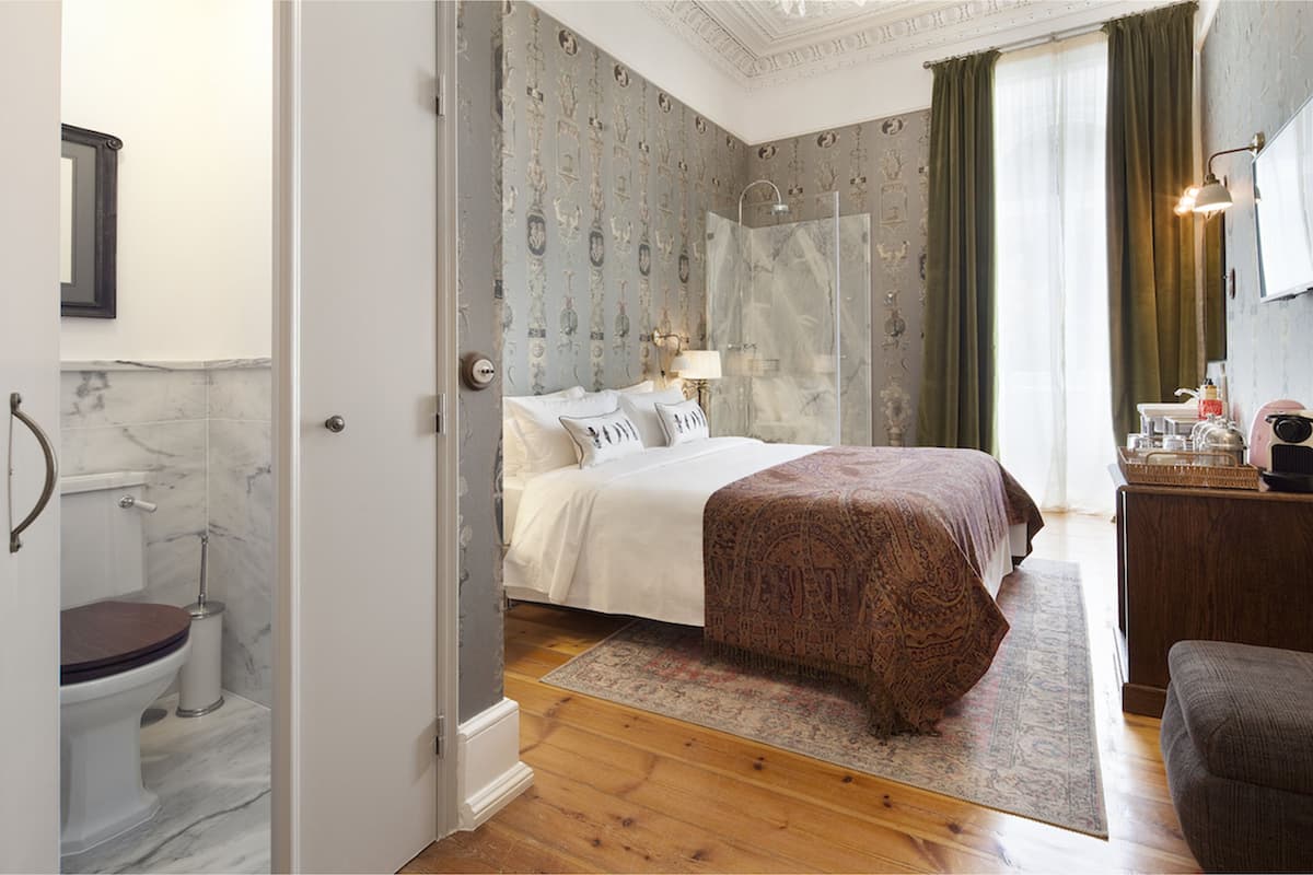 A bedroom with a bed, a bedside table, a mirror, and a bathroom visible through an open door.