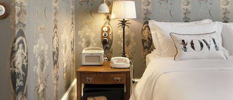 A bedroom with a bed, a nightstand with a lamp, a vintage radio, and a telephone.
