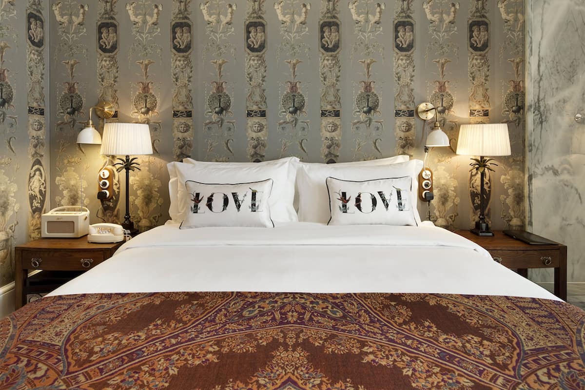 A hotel room with a large bed, two bedside lamps, a nightstand with a telephone, and a patterned carpet.