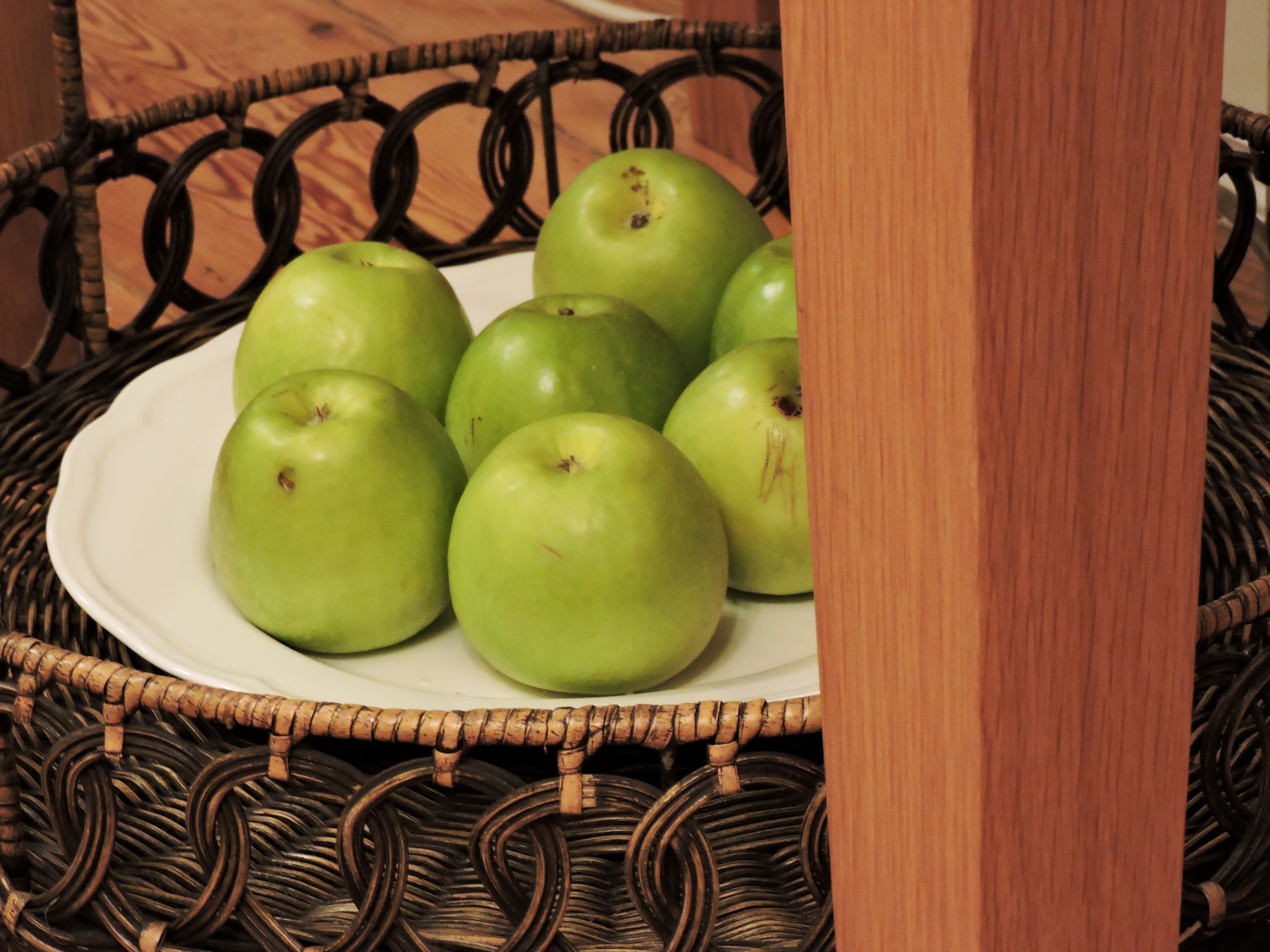 A wicker basket containing a white plate with several green apples.