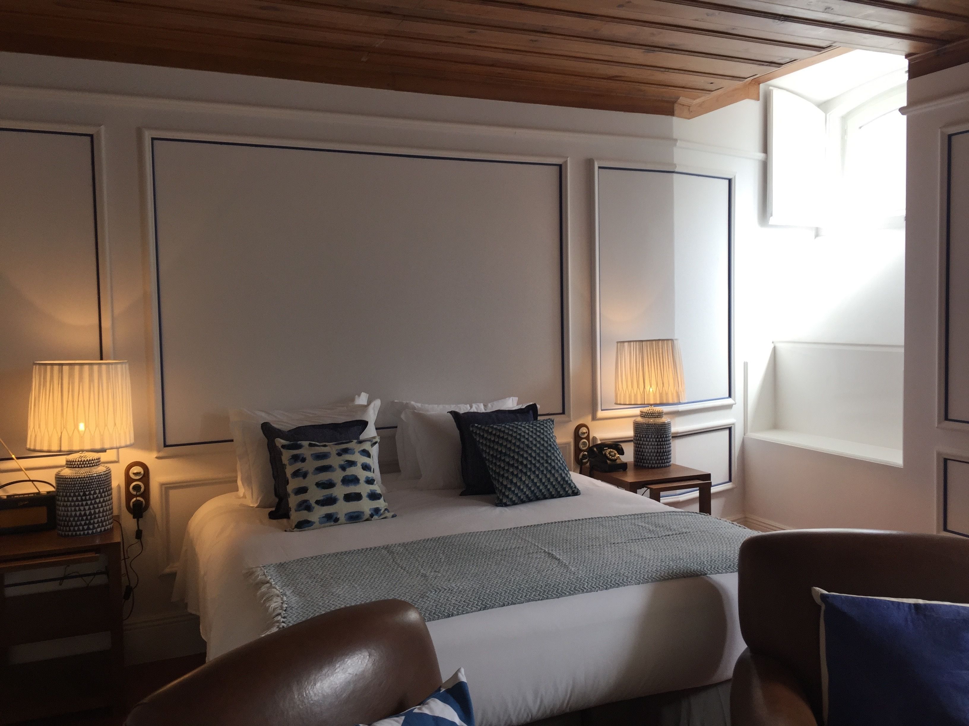 A hotel room with a large bed, two bedside tables, a chair, and a window with natural light.
