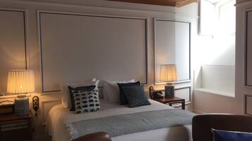 A hotel room with a large bed, two bedside tables, a chair, and a window with natural light.