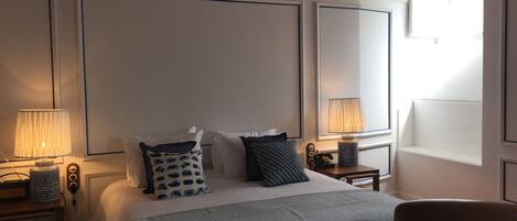 A hotel room with a large bed, two bedside tables, a chair, and a window with natural light.