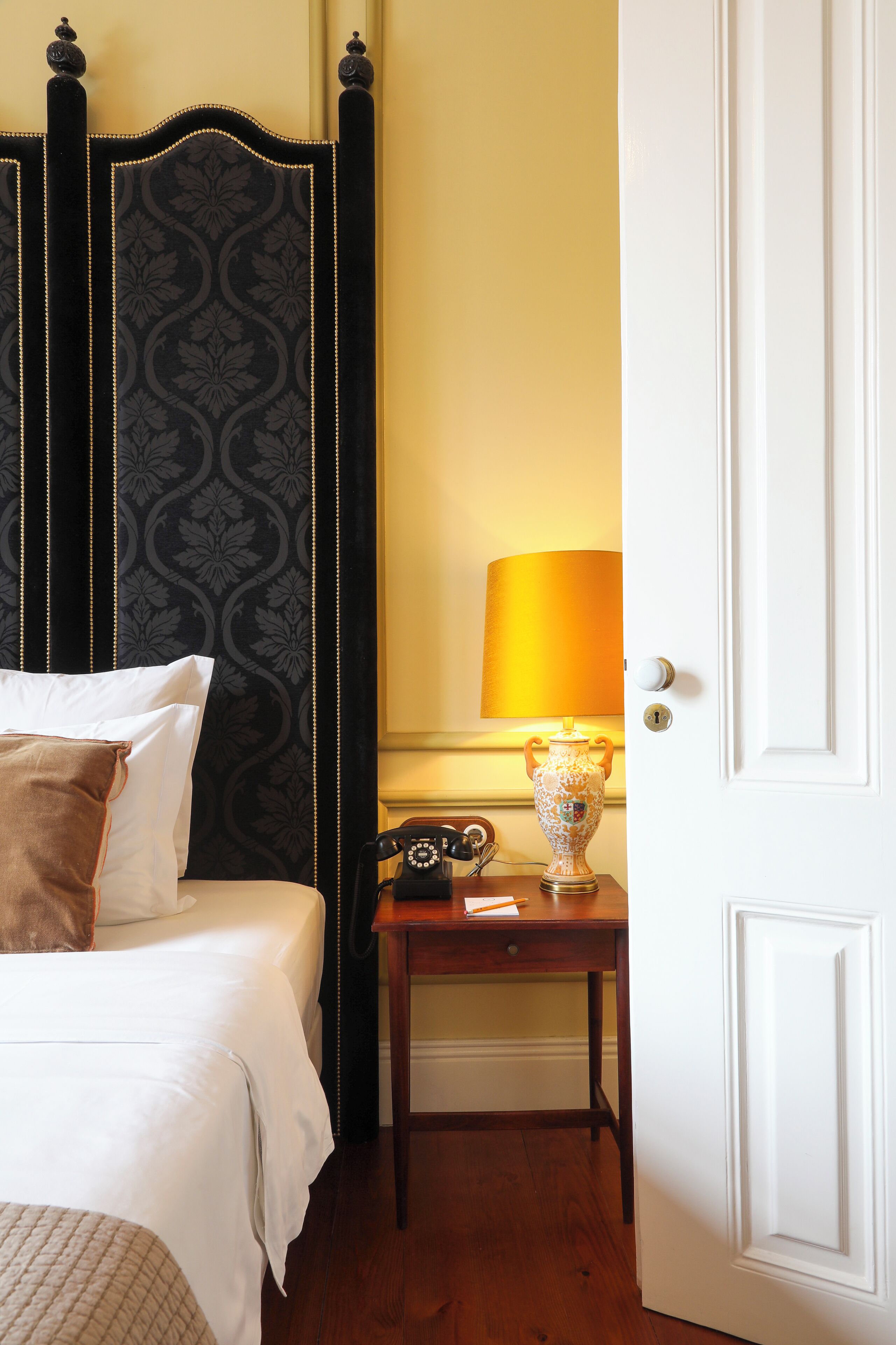 A hotel room with a bed, a bedside table with a lamp, and a door.