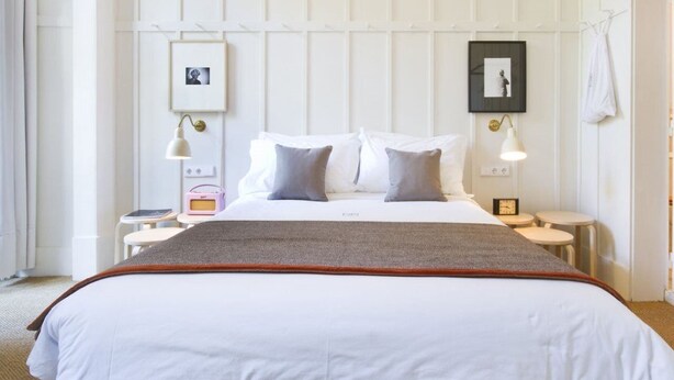 A hotel room with a large bed, two bedside tables, a bedside lamp, a small table with a radio, and a framed picture on the wall.