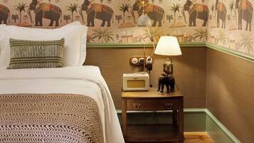 A bedroom with a bed, pillows, a nightstand with a lamp, and a wall with elephant patterns.