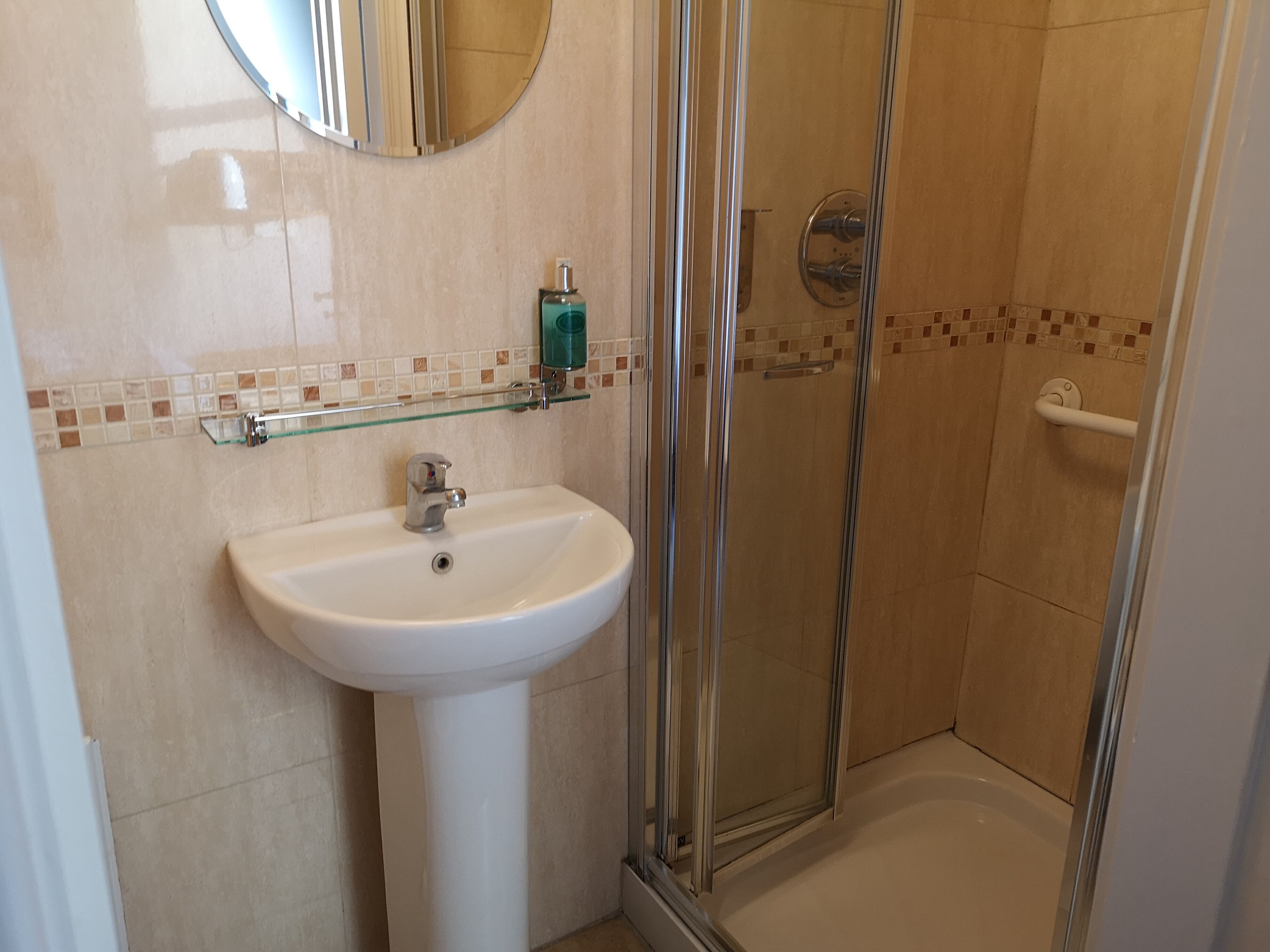 Un baño con lavamanos blanco, cabina de ducha de vidrio y espejo sobre el lavamanos.