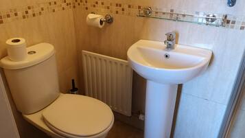 A bathroom with a toilet, a glass shelf with toiletries, and a white sink.