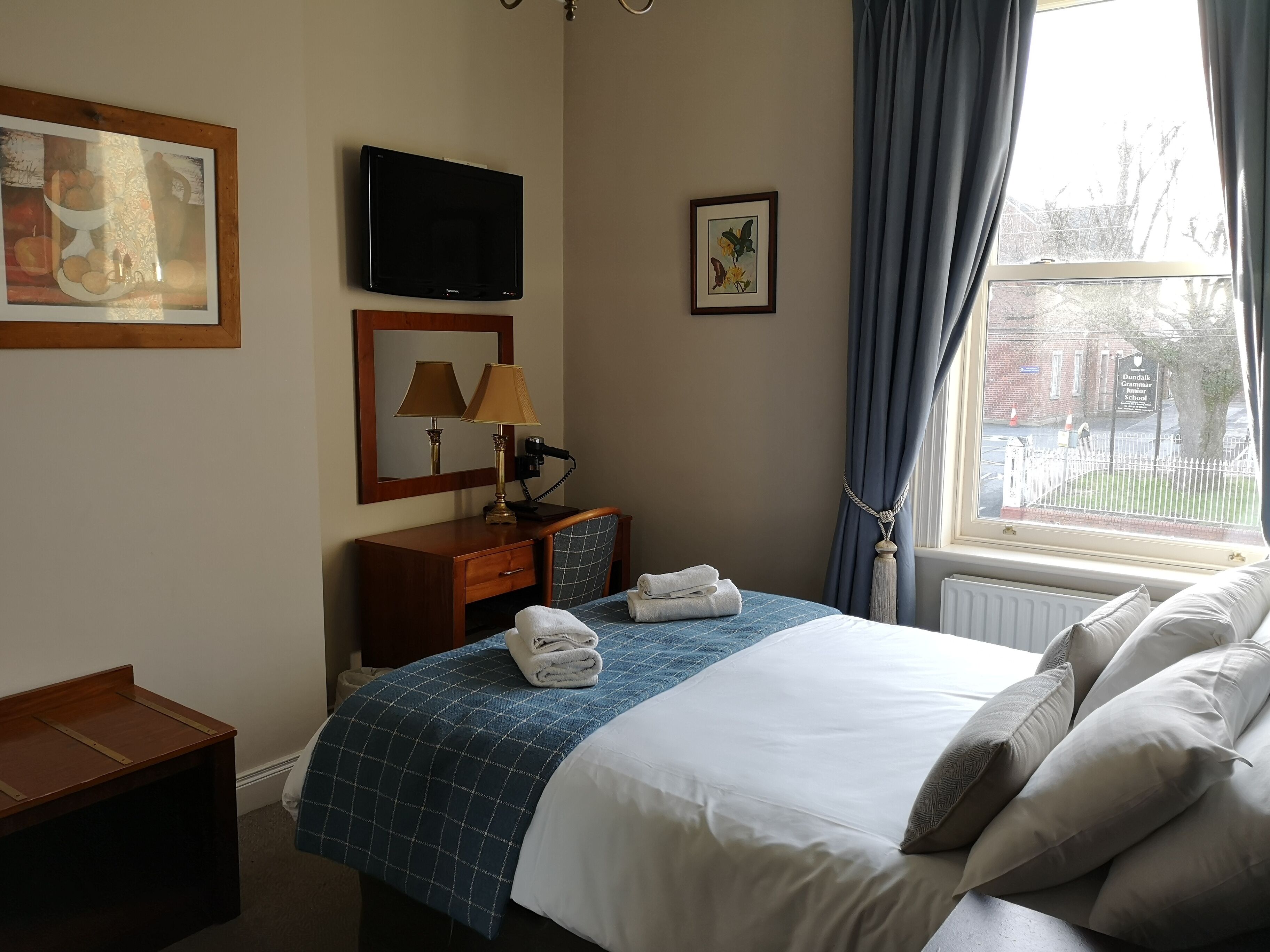 A hotel room with a bed, a desk, a television, and a window with curtains.