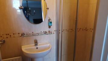 Un baño con un lavamanos blanco, un espejo redondo, una cabina de ducha con mampara de vidrio y un salpicadero de azulejos.