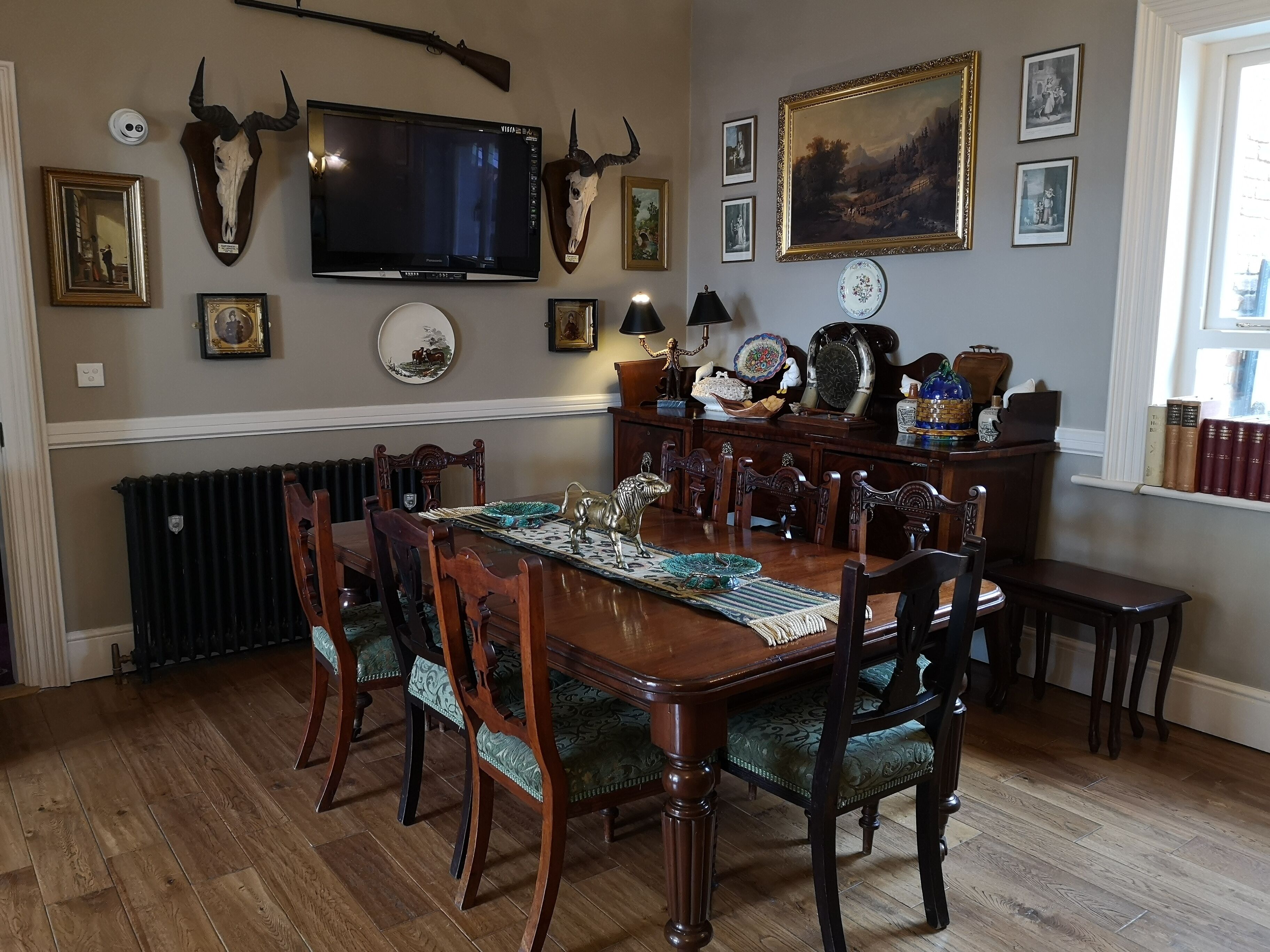 A dining room with a wooden table, chairs, a television, and various wall decorations including framed pictures and a clock.