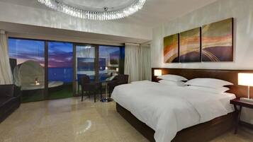 Une chambre d’hôtel dotée d’un grand lit, d’un bureau, d’une chaise et offrant une vue sur le paysage urbain grâce à de grandes fenêtres du sol au plafond.