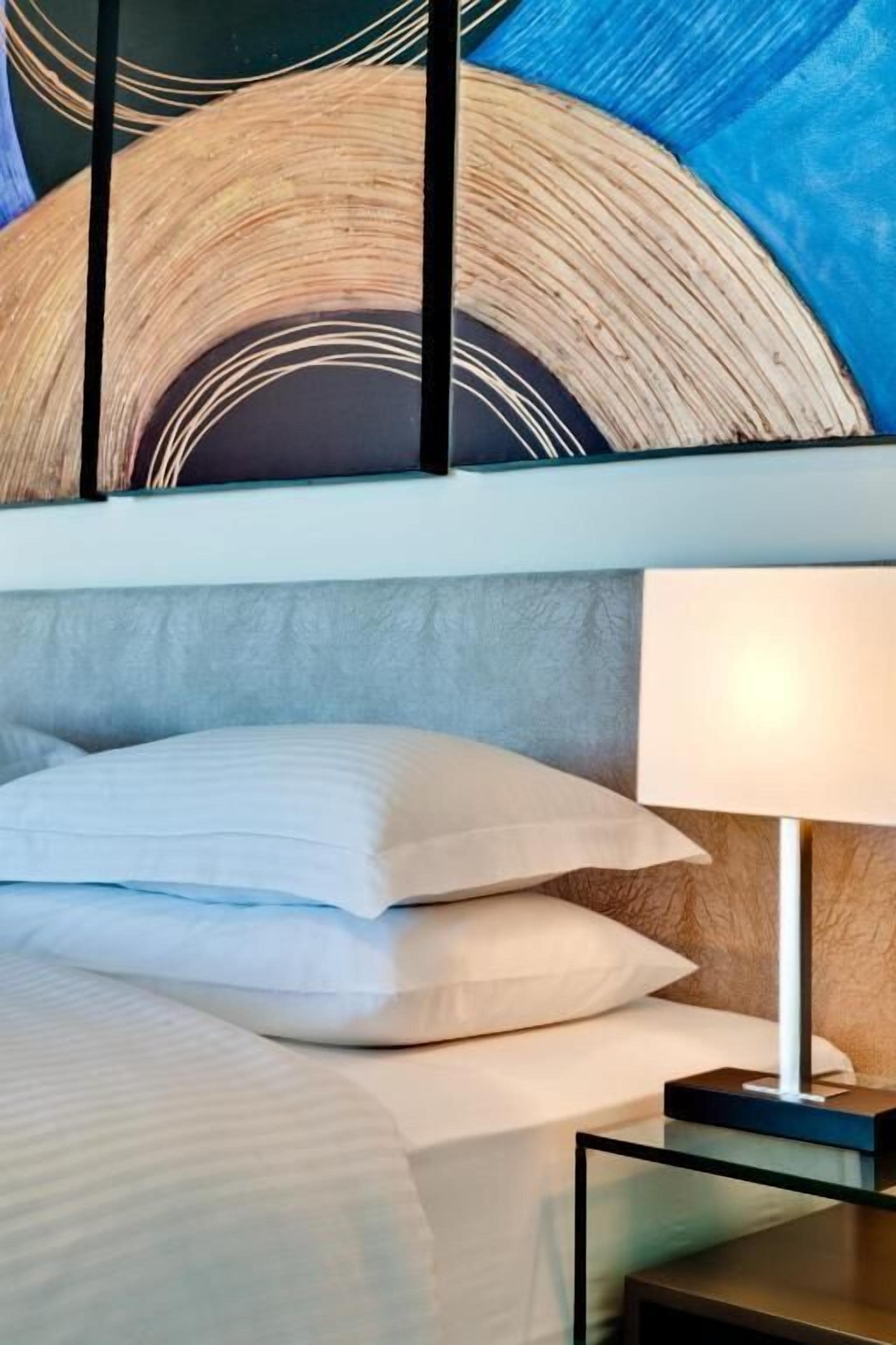 Una habitación de hotel moderna con una cama grande, una mesita de noche con lámpara y una pared con diseño circular.