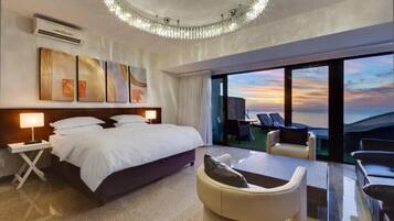 Quarto de hotel com uma cama grande, uma escrivaninha, uma cadeira e varanda com vista para o pôr do sol.